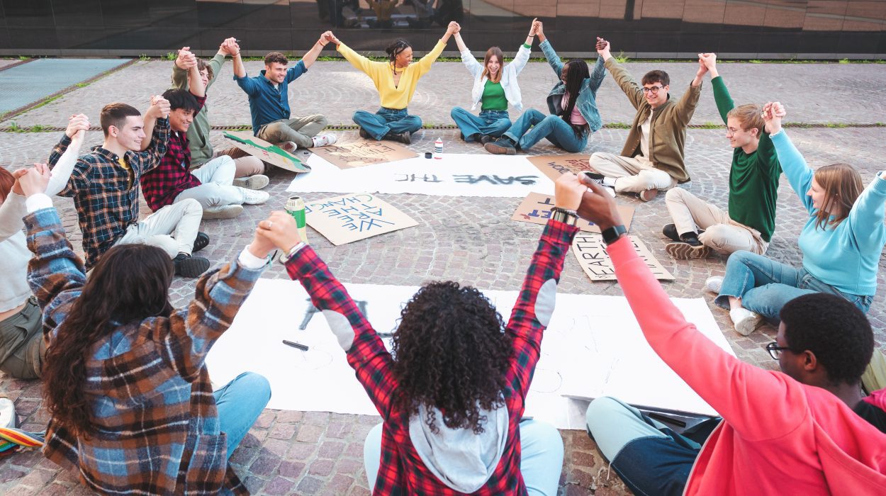 A group of multicultural peacefully activists are sitting with posters outside.