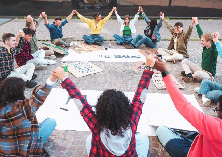 A group of multicultural peacefully activists are sitting with posters outside.