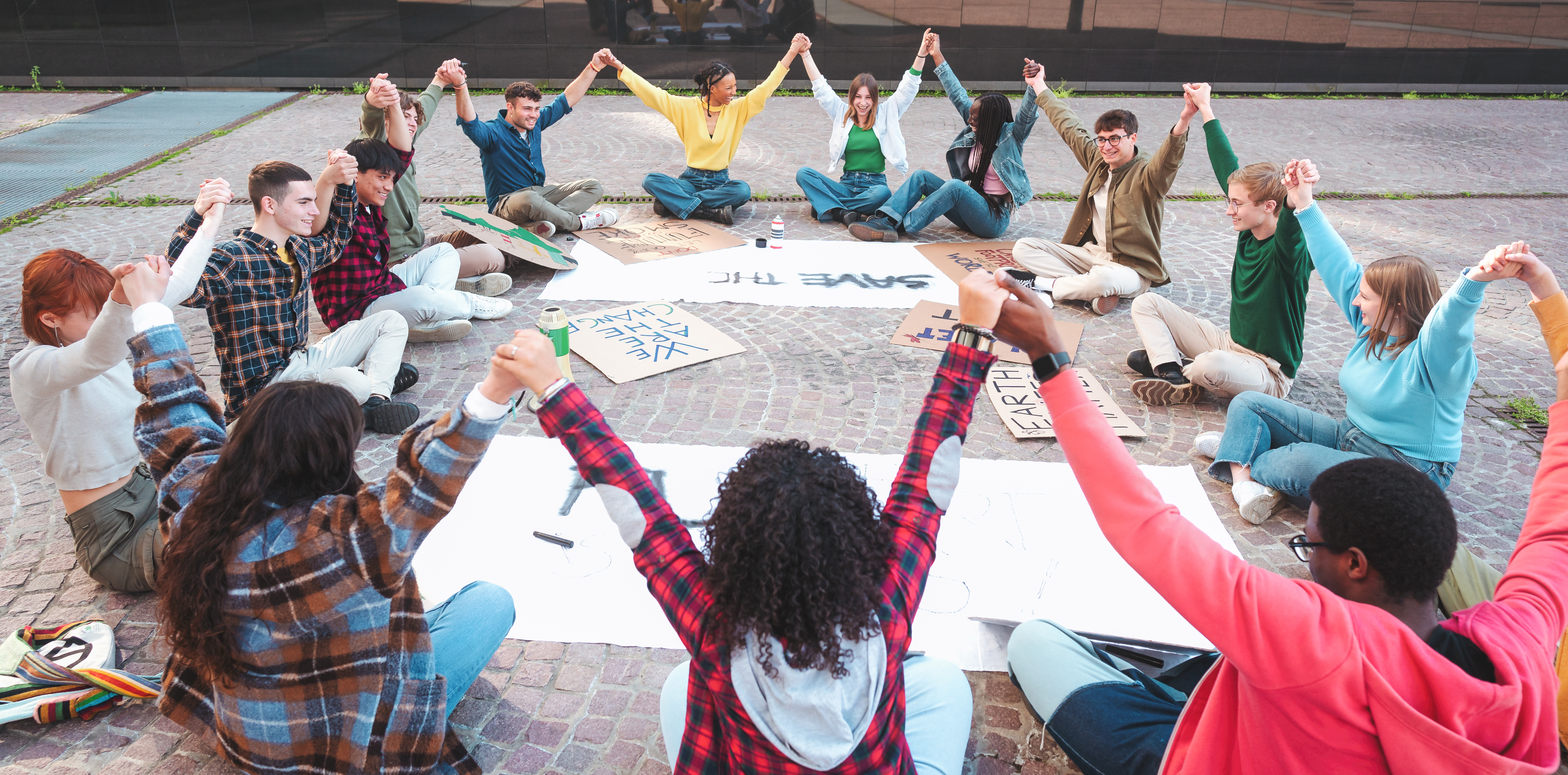 A group of multicultural peacefully activists are sitting with posters outside.